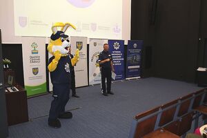 Zdjęcie w kolorze przedstawia salę kinową na środku osoba w przebraniu maskotki opolskiej policji Królik Policuś tuż za nim policjant w mundurze.