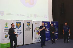 Zdjęcie w kolorze przedstawia salę kinową na środku osoba mówiące do mikrofonu.