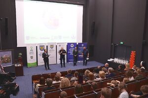 Zdjęcie w kolorze przedstawia salę kinową od strony widowni, na środku osoby mówiące do mikrofonu.