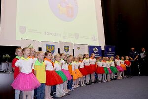 Zdjęcie w kolorze przedstawia salę kinową na środku przedszkolaki wykonujące przedstawienie.