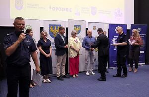 Zdjęcie w kolorze przedstawia salę kinową na środku policjant trzyma mikrofon tuż za nim stoją zaproszeni goście.