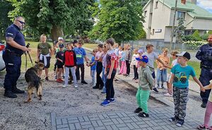 Zdjęcie w kolorze przedstawia policjanta wraz z psem służbowym oraz grupę dzieci