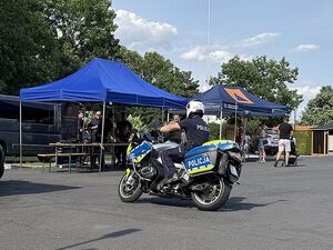 Zdjęcie w kolorze przedstawia policjanta na motocyklu przez stoiskiem promocyjnym.