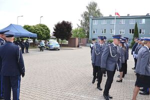 Zdjęcie w kolorze przedstawia zgromadzonych gości stojących z policjantami w umundurowaniu galowym podczas uroczystych obchodów Święta Policji w Oleśnie.