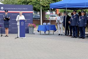 Zdjęcie w kolorze przedstawia Panią Starostę Oleskiego  stojąca przy mównicy, w tle ściana z płótna oraz zgromadzeni goście, podczas uroczystych obchodów Święta Policji w Oleśnie.