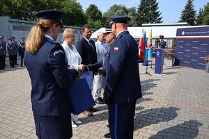 Zdjęcie w kolorze przedstawia pełniącego obowiązki Komendanta Powiatowego Policji w Oleśnie oraz Zastępcę Komendanta Wojewódzkiego Policji w Opolu podczas wręczania podarunków wyróżnionym gościom.