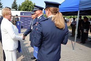Zdjęcie w kolorze przedstawia pełniącego obowiązki Komendanta Powiatowego Policji w Oleśnie oraz Zastępcę Komendanta Wojewódzkiego Policji w Opolu podczas wręczania podarunków wyróżnionym gościom.