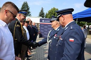 Zdjęcie w kolorze przedstawia pełniącego obowiązki Komendanta Powiatowego Policji w Oleśnie oraz Zastępcę Komendanta Wojewódzkiego Policji w Opolu podczas wręczania podarunków wyróżnionym gościom.