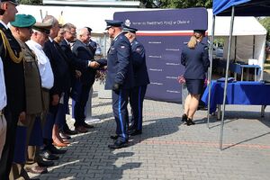 Zdjęcie w kolorze przedstawia pełniącego obowiązki Komendanta Powiatowego Policji w Oleśnie oraz Zastępcę Komendanta Wojewódzkiego Policji w Opolu podczas wręczania podarunków wyróżnionym gościom.