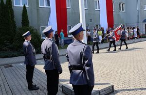Zdjęcie w kolorze przedstawia policjantów Pocztu Flagowego  oddającego honory w tle Poczet Sztandarowy i stojący za nim goście.