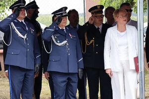 Zdjęcie przedstawia policjantów oddających honory w tle uczestnicy Święta