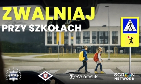 Zdjęcie w kolorze przedstawia dzieci idące po przejściu dla pieszych, po lewej napis Zwalniaj przy szkołach.