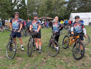 Zdjęcie w kolorze przedstawia policjantów w strojach sportowych stojących jeden obok drugiego z rowerami przy boku, w tle pozostali uczestnicy wydarzenia.