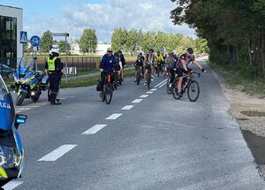 Zdjęcie w kolorze przedstawia policjantów ruchu drogowego którzy stoją na jezdni, obok nich przejeżdżają uczestnicy rajdu.