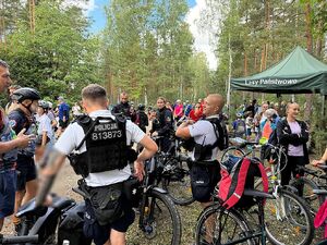 Zdjęcie w kolorze przedstawia policjantów drużyny rowerowej  podczas przerwy z innymi uczestnikami  rajdu podczas przerwy w obszarze leśnym.