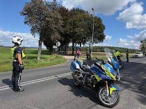 Zdjęcie w kolorze przedstawia policjantów ruchu drogowego którzy stoją na jezdni, obok nich przejeżdżają uczestnicy rajdu.