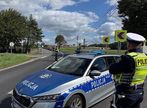 Zdjęcie w kolorze przedstawia policjantów ruchu drogowego którzy stoją na jezdni, obok nich przejeżdżają uczestnicy rajdu.