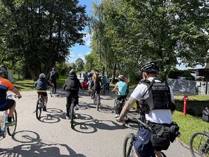 Zdjęcie w kolorze przedstawia uczestników rajdu jadących po jezdni, po prawej policjant z drużyny rowerowej.