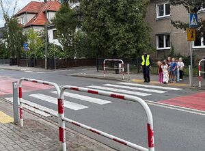 zdjęcie przedstawia policjanta przeprowadzającego dzieci przez przejście dla pieszych.