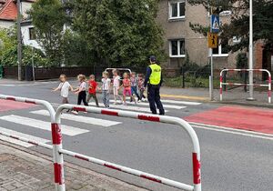 zdjęcie przedstawia policjanta przeprowadzającego dzieci przez przejście dla pieszych.