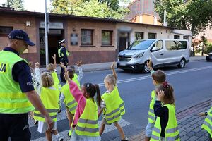 zdjęcie przedstawia policjanta przeprowadzającego dzieci przez przejście dla pieszych.