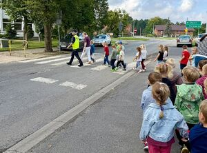 Zdjęcie przedstawia grupę dzieci przechodzace przez przejście dla pieszych z policjantką.