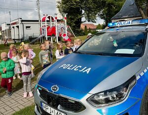 Zdjęcie przedstawia grupę dzieci stojżcych przy radiowozie