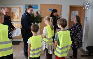 Zdjęcie przedstawia policjantów wraz z dziećmi w kamizelkach odblaskowych w budynku KPP, dzieci wręczają kwiaty dla policjantek.