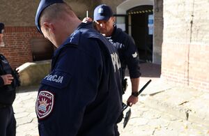 Zdjęcie przedstawia policjantów stojących przed budynkiem szkoły.