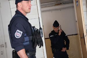 Zdjęcie przedstawia policjantów w pomieszczeniu, jeden trzyma przy twarzy radiostację.