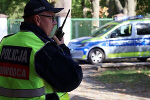 Zdjęcie przedstawia policjanta w kamizelce dowódca akcji trzymającego przy ustach radiostację