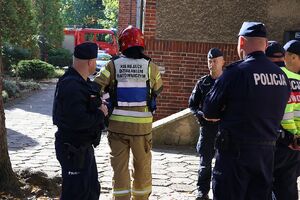 Zdjęcie przedstawia policjantów i dowódcę strażaka w tle czerwony wóz strazy pozarnej.