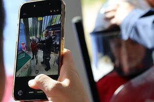 Na zdjęciu widać telefon komórkowy oraz stojących  dwóch umundurowanych policjantów demonstrujących sprzęt policyjny chłopcu.