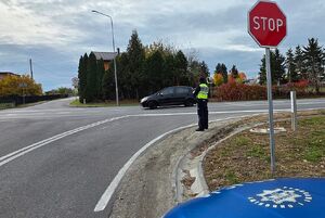 Zdjęcie przedstawia policjanta ruchu drogowego z miernikiem prędkości w rejonie skrzyżowania.