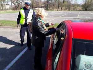 przedstawicielka stowarzyszenia Nasza Szansa wręcza kierującemu opaskę odblaskową i długopis w tle stoi uśmiechnięty policjant