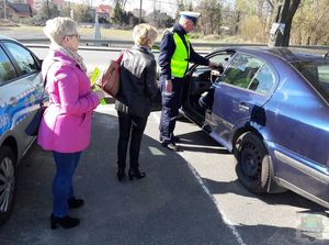 policjant prowadzi kontrole trzeźwości kierującego obok stoją przedstawicielki stowarzyszenia nasza szansa z upominkami w postaci odblasków i długopisów.