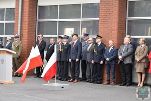 Przedstawiciele władz samorządowych i służb mundurowych stoją w szeregu, w tle budynek straży pożarnej w Oleśnie