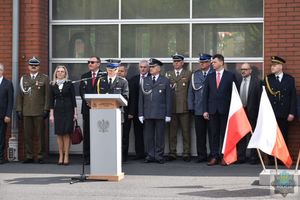 Przedstawiciele władz samorządowych i służb mundurowych stoją w szeregu, w tle budynek straży pożarnej w Oleśnie