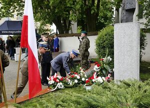 Komendant Powiatowy Policji w Olesnie insp. Tomasz Kubicki składa wieniec pod pomnikiem Papieża Jana Pawła 2 obok przedstawiciel Wojska Polskiego w tle mieszkańcy Olesna