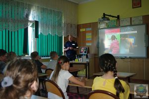 Policjant zajmujący się profilaktyką  społeczną prowadzi pogadankę na temat przemocy w internecie. Dzieci oglądają wyświetlony na tablicy interaktywnej slajd.