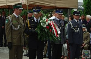 Przedstawiciele służb mundurowych składają wiązankę biało-czerwonych kwiatów na płycie pomnika Powstańców Śląskich