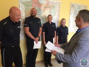 Dwaj policjanci i dwie policjantki  stoją w szeregu pod ścianą. 1 Zastępca KWP insp. Adam Tychowicz stoi przed pierwszym od lewej funkcjonariuszem, trzyma w ręku pisemne nagrody. Wszyscy się uśmiechają.