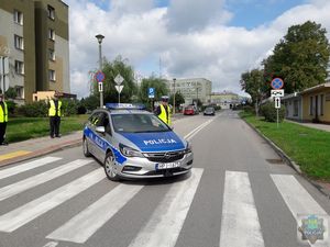 Droga dojazdowa do szpitala zablokowana przez oznakowany pojazd policyjny, obok stoi funkcjonariusz policji, po lewej stronie na chodniku stoją dwaj funkcjonariusze straży mieskiej, w oddali budynek szpitala rejonowego w oleśnie.