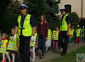 Dwóch policjantów ruchu drogowego prowadzi wspólnie z wychowawcami grupę dzieci na przejście dla pieszych