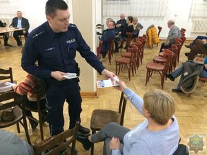 Policjant wręcza uczestnikom spotkania gadżety powiązane z akcją świadomy i bezpieczny senior.