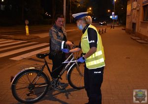 Policjantka ruchu drogowego zakłada odblaskowa opaskę na ręce rowerzysty.