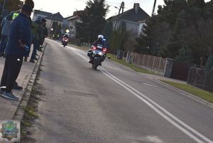 Policjanci pilotujący na 2  motocyklach jadą ul. Wachowską  zbiżają się do końca wyścigu. Po lewej stronie na chodniku osoby kibicujące.