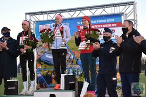 Podium na stadionie miejskim w oleśnie, na podium udekorowane  najlepsze zawodniczki.  Przy podium przedstawiciele władz lokalnych o służb mundurowych. Tło utworzone z banera reklamującego Maraton oleski.