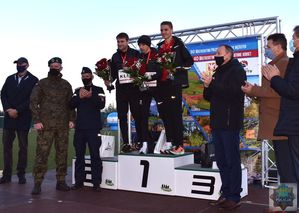 Podium na stadionie miejskim w oleśnie, na podium udekorowani  najlepsi zawodnicy.  Przy podium przedstawiciele władz lokalnych i służb mundurowych. Tło utworzone z banera reklamującego Maraton oleski.