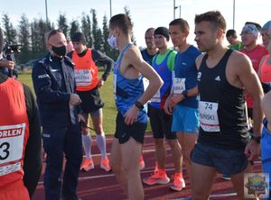 Zawodnicy - biegacze zgrupowani na czerwonym tartanie bieżni lekkoatletycznej. pośród nich umundurowany funkcjonariusz - Komendant 
Powiatowy Policji w Oleśnie - insp. Tomasz Kubicki.